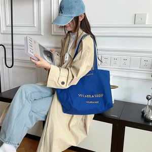 Makroaufnahme der großen blauen Canvas-Tasche mit gesticktem Gold-Schriftzug und Textur