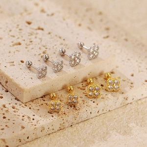 Detailed view of silver and gold clover earrings with zircons on beige stone