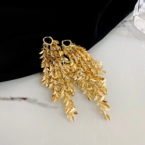 Close-up of golden leaf tassel earrings with metallic texture on white marble surface