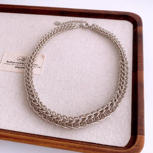 Détail d'un collier chaîne argentée avec tissage multi-maillons sur plateau bois