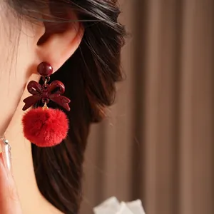 Deep red bowknot earrings with plush fur balls on model for elegant winter style