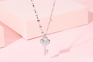 Close-up of silver key pendant with white shell inlay and crystals in a pink gift box