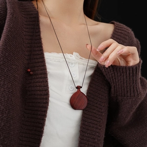 Close-up of a vintage wood flask pendant on a braided cord worn with a cardigan