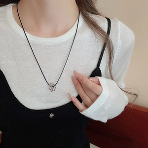 Close-up of a silver daisy flower pendant on a thin black cord worn by a model