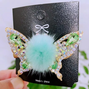 Detail of a gold butterfly hair clip with green crystals and soft pompom embellishments