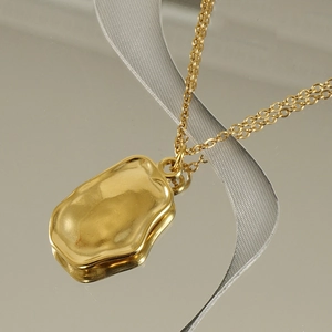 Detailed macro view of a gold rectangular pendant with irregular lava-style wave texture