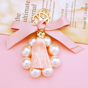 Detail of pink fabric bow keychain with white faux pearls and elegant fringe tassel
