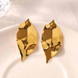 Detail of 18k gold wrinkled leaf stud earrings displayed on white ceramic plate