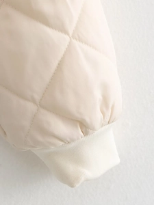 Détail du matelassage en losanges et des poignets en tricot côtelé sur un bomber crème