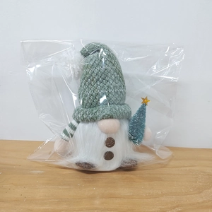 Detail of a plush Christmas gnome with green knit hat and gold star tree in clear polybag
