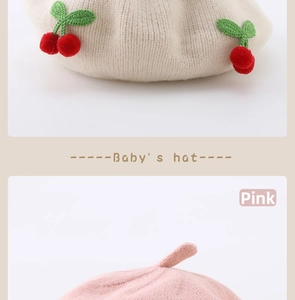 Close-up of baby knit beret with cherry decor and pink textured woolen fabric