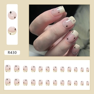 Dettaglio macro di unghie finte corte riutilizzabili con stelle nere su base beige