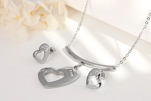 Elegant silver heart necklace and earrings set with small diamonds on white background