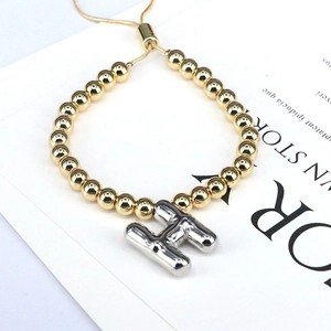 Detail of beaded gold bracelet with silver balloon H pendant and adjustable chain