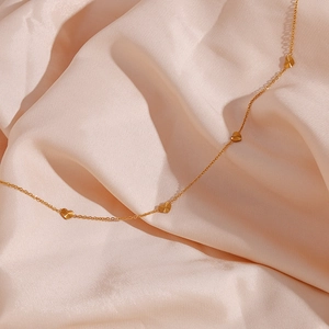 Detailed view of multiple gold heart charms on a delicate necklace over silk fabric
