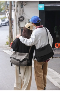 Street style shot of black and grey canvas messenger bags shown from a back view