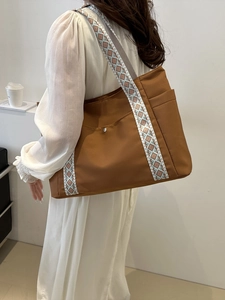 Borsa tote marrone con tracolla geometrica indossata da modella in abito bianco