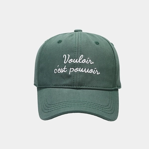 Detailed embroidery of the French quote on a green cotton baseball cap