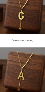 Detail view of gold letter G and A pendants on fine titanium steel chain on wooden stand