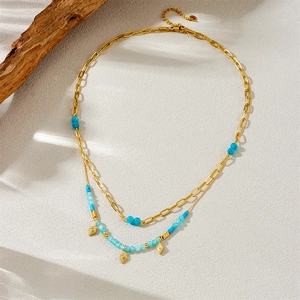 Gold layered stainless steel necklace with blue beads and geometric pendant on beige