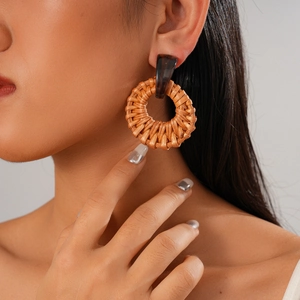 Close-up of bohemian style round woven rattan earrings worn by a model on grey background