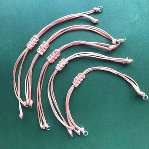 Detail view of five adjustable light pink braided wax cord bracelets with metal ring charms
