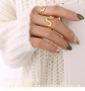 Close-up of dual gold wavy stacking rings on fingers with white knit texture background