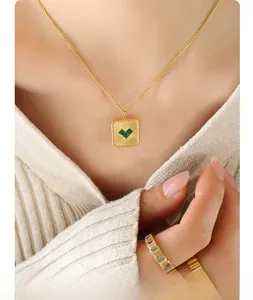 Close-up of a gold square pendant necklace with a green heart-shaped stone on a model