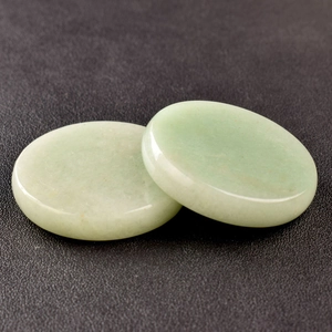Macro view of light green round jade stone discs on black textured leather surface