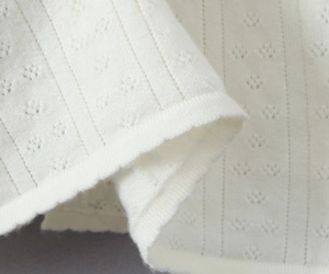 Vue macro du tissu en maille crème avec motifs ajourés et finition à bords roulés