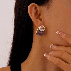 Detailed close-up of a golden flower earring with pearls and purple beads on a model