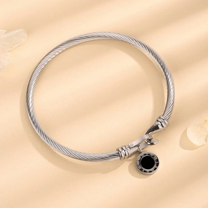 Silver twisted cable bracelet featuring a black Roman numeral charm on a warm background