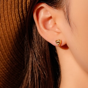 Close-up of small golden heart earring with red zircon detail worn on a model's ear