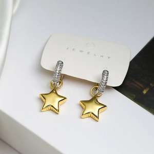 Close-up of asymmetric gold star pendant earrings with silver zircon stones on jewelry card