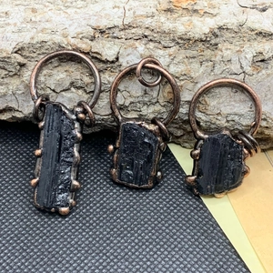 Dettaglio macro di tre ciondoli in tormalina nera grezza con bordi ramati galvanizzati