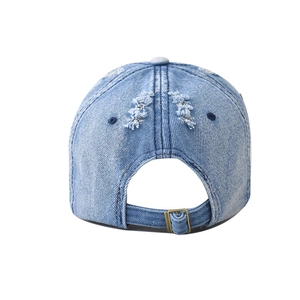 Detail of washed denim baseball cap featuring distressed holes and metal adjustment buckle