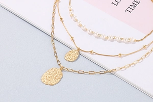 Close-up of multilayered gold necklace set with pearls and hammered oval pendants