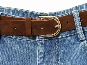 Close-up of a brown suede belt with polished gold metal buckle on blue high-waist denim pants