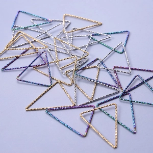 Macro shot of 18k gold and silver geometric triangle charms for DIY jewelry on violet background