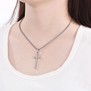 Close-up of a silver polished stainless steel cross pendant on a box chain worn by a model