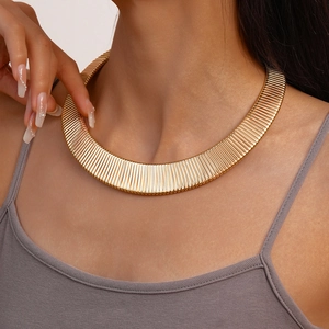 Close-up of a wide gold metal choker necklace with ribbed texture on a model neck