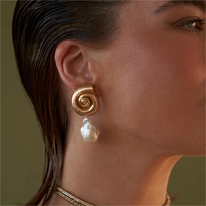 Close-up of golden spiral conch earrings with baroque pearls worn by a model