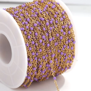 Detailed macro view of golden stainless steel DIY chain with purple enamel beads on a spool