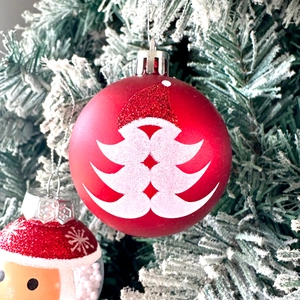 Detail view of a 6cm red Christmas ball with glitter and Santa motifs on snowy pine branch