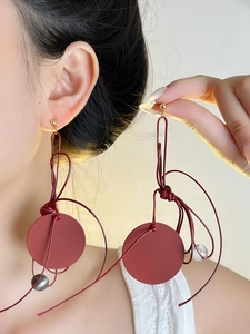 Close-up of elegant burgundy round drop earrings with golden studs and woven cord