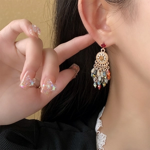 Detail of floral gold earrings with colorful crystal beads and flowing tassels on a model