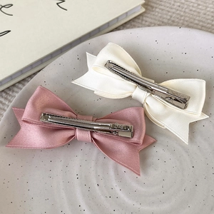 Detail view of pink and beige satin bow hair clips with Korea engraved metal duckbill base