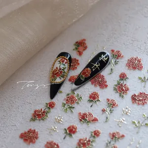 Détail de stickers à fleurs rouges et calligraphie dorée sur ongles stiletto noirs