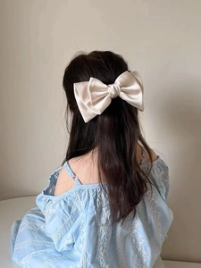 Detail of cream satin oversized bow hair clip worn on long straight hair for girls