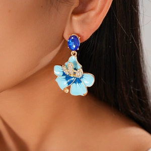 Detail of blue enamel flower earrings with gold finish and zircon stones on a model